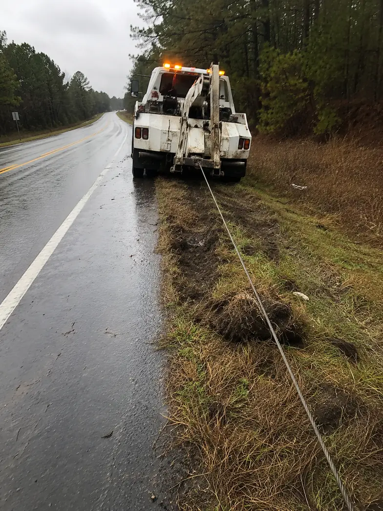 Tow truck winching a pickup out of a muddy roadside ditch near Atascocita